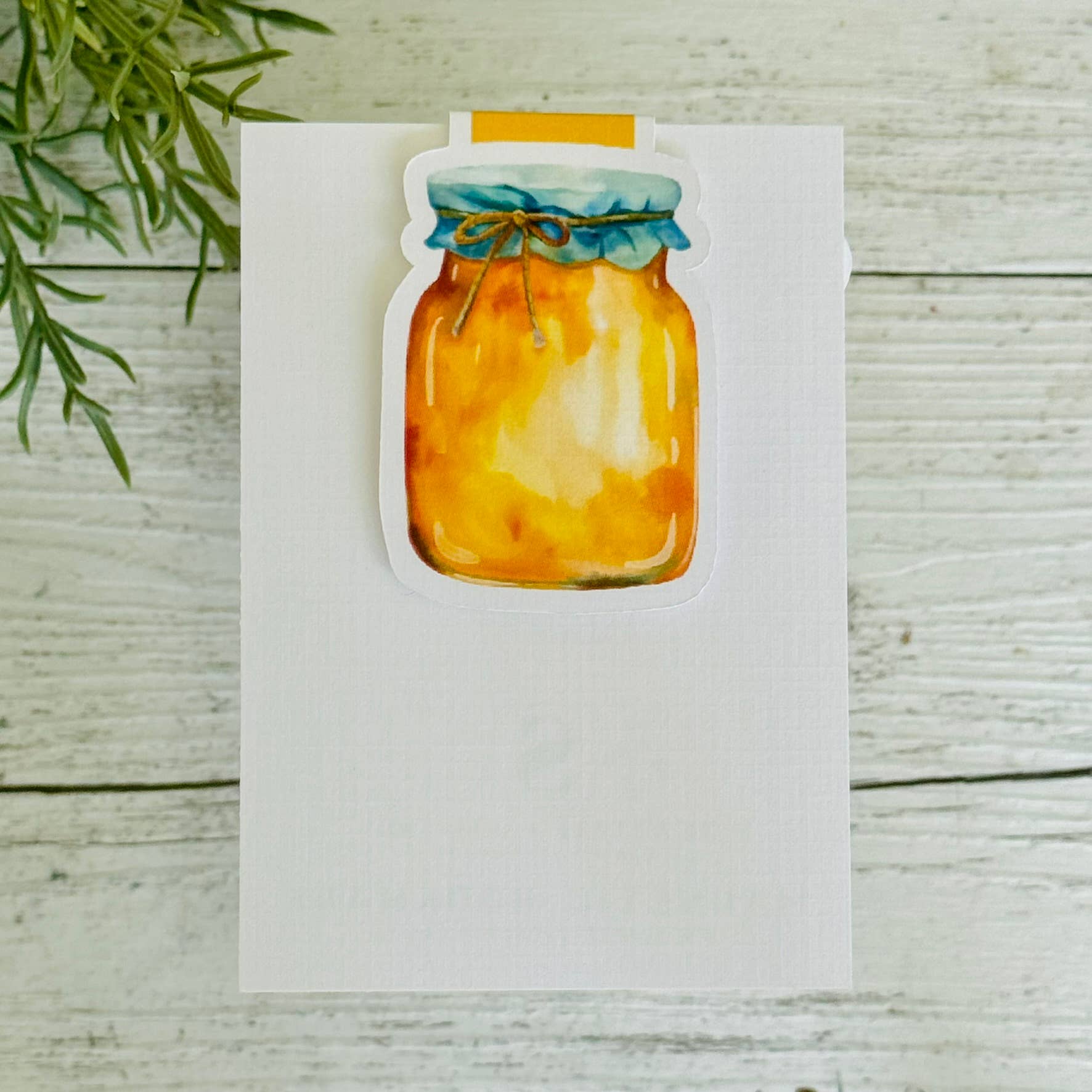 Sticker of a jar with a blue lid on a white card with a wooden background